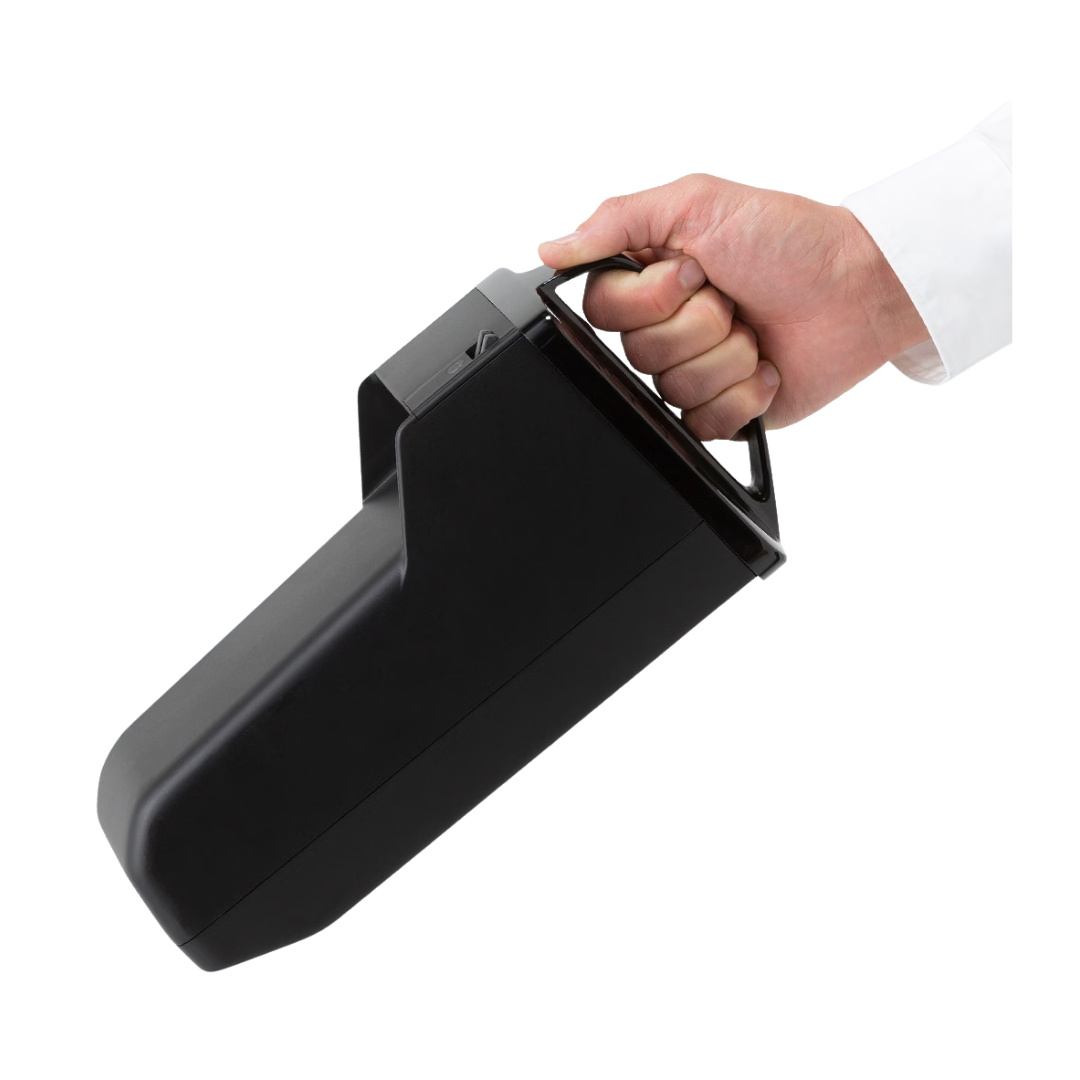 A person in a white sleeve holds the Extra Battery for WHILL C2 and F Model Power Chairs—a large, black, rectangular device with a handle—demonstrating its travel-friendly mobility against a white background.
